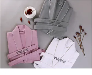 Detailansicht von Waffel-Baumwoll-Bademänteln in Grau, Rosa und Weiß mit feiner Stickerei.