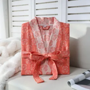 Double-gauze cotton bathrobe neatly folded on sofa, showcasing floral print and waist belt.