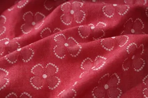 Red cotton double-gauze fabric close-up with white clover pattern texture detail.