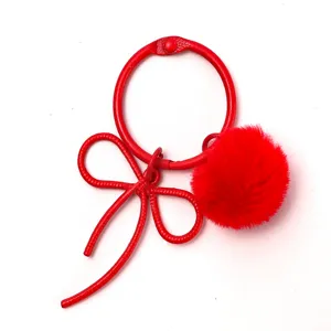 Red metal binder ring keychain with cute bow and fluffy pom-pom pendant for bag decoration.