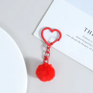 Détail en gros plan d'un porte-clés pompon pelucheux rouge avec fermoir métallique en cœur.