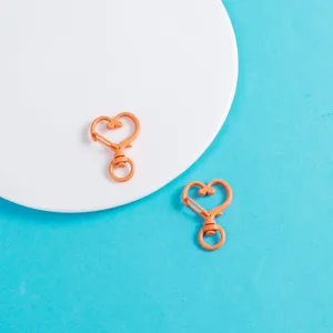 Gros plan détaillé de mousquetons en forme de cœur orange, accessoires de bijoux DIY.