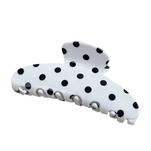 Detailed close-up of the white polka dot hair claw clip, showing acrylic surface texture.