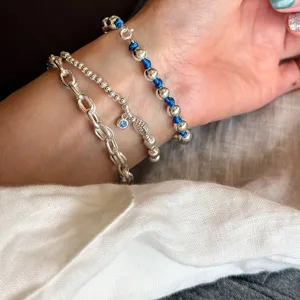 Detailopname van gestapelde zilveren armbanden met blauwe kralen en ketting schakels.