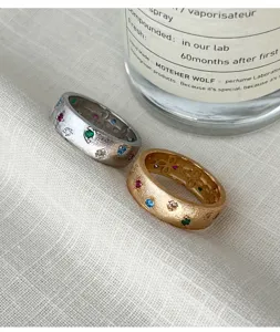Détail en gros plan des bagues larges texturées en zircon multicolore argent et or.