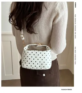 Lifestyle detail of white polka dot cosmetic bag featuring gold hardware and strap.