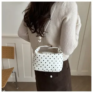 Portable white polka dot cosmetic bag detail view, stylish leather handbag with shoulder strap.