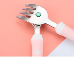 Close up of stainless steel toddler fork and spoon set with cute pink handle and green gem detail.