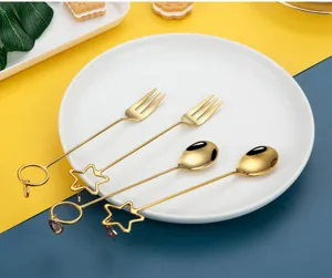 Gold stainless steel dessert spoon and fork set detail, featuring cute ring and star charms.