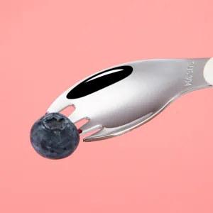 304 stainless steel kids fork spoon set holding fresh blueberry on pink background.