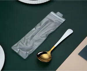 Detail view of a stainless steel gold round spoon with white handle and transparent storage bag.