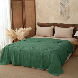 Detail shot of the solid green cotton gauze blanket displayed neatly on a cozy bed, soft texture.