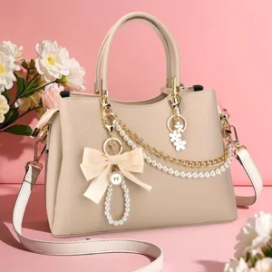 Elegant detail van de stijlvolle beige lederen handtas met parelketting en bloemhanger.
