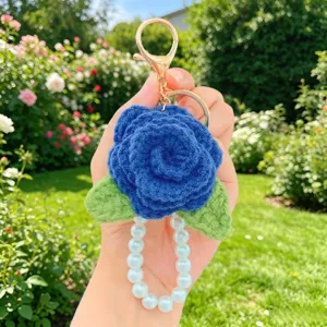 Nahaufnahme des handgefertigten blauen Häkel-Rosen-Schlüsselanhängers mit weißen Perlen.