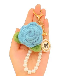 Detailansicht des handgefertigten blauen Häkel-Rosen-Schlüsselanhängers mit eleganter Perlenkette.