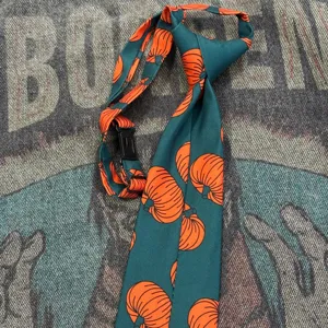 Close-up view of the dark green necktie featuring a playful orange pumpkin print pattern.