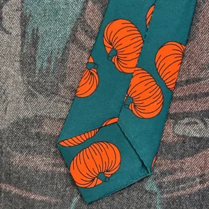 Close-up detail of dark green necktie featuring vibrant orange pumpkin pattern design.