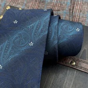 Dettaglio in primo piano di cravatta blu sfumata in jacquard paisley arrotolata su legno.