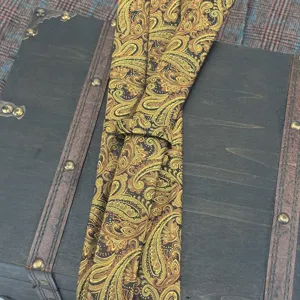 Detail shot of a luxurious yellow-green paisley jacquard necktie featuring intricate vintage patterns.