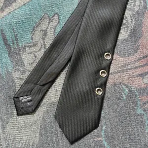 Detail shot of black punk style tie featuring three metal eyelets and handmade polyester quality.