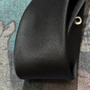 Close-up detail of black punk style tie featuring premium twill fabric and metallic eyelet decor.