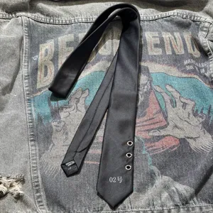 Dark punk style black necktie featuring metal eyelet details and number print close up.