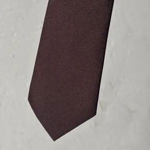 Primer plano detallado de una elegante corbata tejida marrón, ideal para atuendos vintage y de estudiantes.
