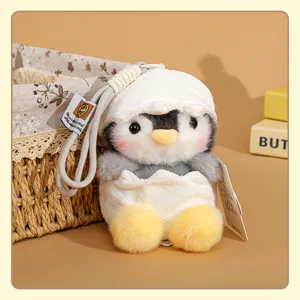 Detalle de colgante de peluche de pinguino en cascara de huevo, juguete suave con cordon trenzado.