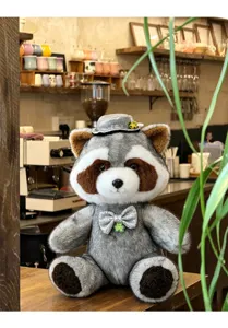 Detailed shot of the cute gentleman raccoon plush toy in a warm cafe scene setting nicely.