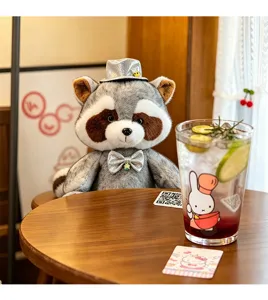 Detail view of the cute gentleman raccoon plush toy sitting on a cozy cafe wooden table.
