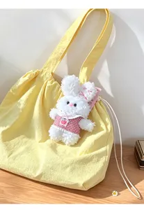 Cute bunny plush doll pendant detail, soft fluffy rabbit toy hanging on a yellow canvas tote bag.