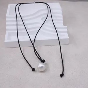 Gros plan détaillé d'un simple collier en cuir noir avec un grand pendentif perle blanche.