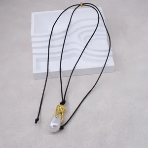 Vue détaillée du collier de perles baroques avec embout en métal doré sur cordon noir.
