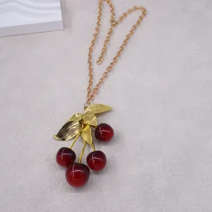 Goldfarbene Kette mit rotem Kirschen-Anhänger Detailaufnahme, elegantes Schmuckaccessoire.