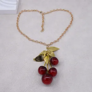 Elegante goldfarbene Kette mit rotem Kirschen-Anhänger und strukturierten Blättern.