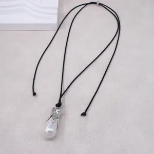 Détail d'un long collier à cordon noir avec embout métallique argenté et pendentif perle.
