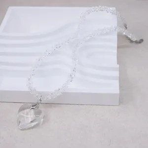 Detailed shot of a clear crystal heart pendant necklace with beaded chain on a white display.