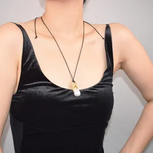 Long collier de perles imitation baroque avec fermoir en métal doré et cordon noir.