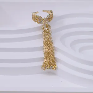 Close-up of golden bow open ring with long chain tassel, sparkling cubic zirconia details.