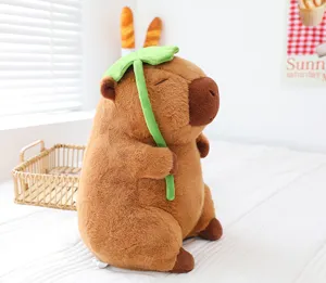 Close-up of cute capybara plush toy holding green leaf, sitting on soft cozy bedroom bed.