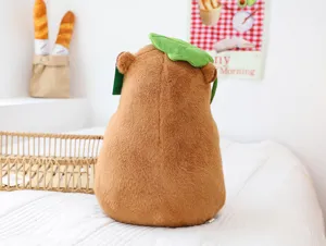 Cute capybara plush toy with green leaf hat, soft stuffed animal doll for hugging room decor.