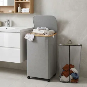 Cesto portabiancheria in tessuto grigio con bordo in legno, coperchio e ruote in un bagno moderno.