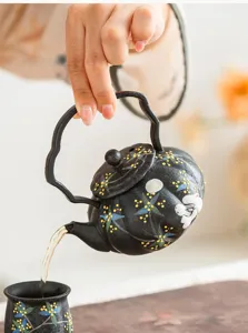 Close-up detail of handcrafted ceramic teapot with rabbit and floral motifs pouring hot tea.