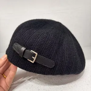 Close-up of black knitted beret detail featuring a chic leather strap and metal buckle.