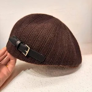 Close-up detail of brown knitted beret, featuring side PU leather strap and metal buckle.