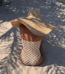Stunning strapless one-piece swimsuit with floral print and wide-brim hat on a sunny beach.
