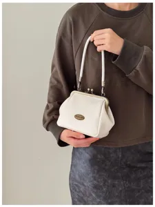 Detail view of a vintage white kiss-lock mini handbag with bronze hardware and hand badge.