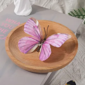 Gros plan détaillé d'un papillon artificiel 3D rose placé dans un petit bol en bois décoratif.
