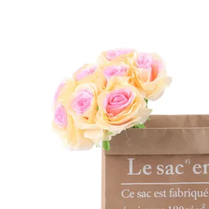 Artificial rose flower bouquet detail, multi-head pink and yellow fake roses in paper bag.