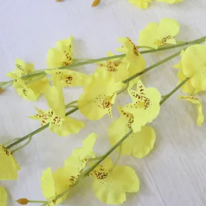 Detailed close-up view of artificial yellow dancing orchid silk flowers with brown spots.